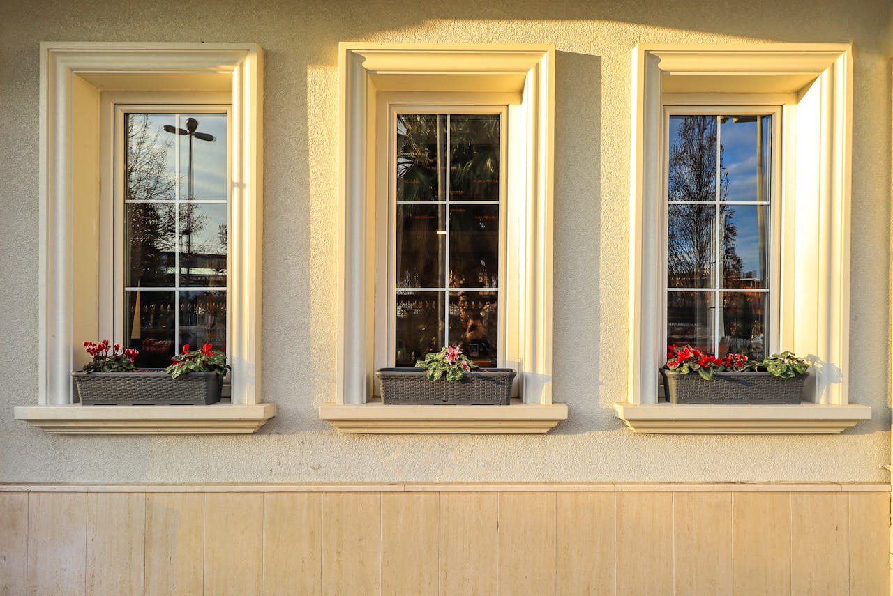 Elegant building facade featuring three windows with vibrant flowerpots on the sills at sunset.